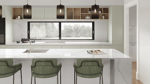 A modern kitchen layout features a marble-look quartz island, countertop, and backsplash, which flanks a large window with a view of the treetops.
